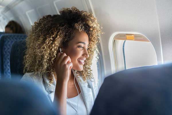 Mulher em um avião olhando pela janela ajustando o fone de ouvido
